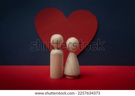 Two wooden peg dolls couple standing before red heart with navy and red background. Love, romantic, Valentine's Day.