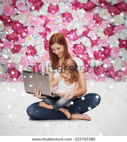 childhood, parenting, people and technology concept - happy mother with little girl with laptop computer over wooden floor and flowers background