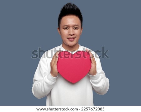 Handsome man holding red heart shape with both hands
