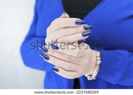 Female beautiful hand with long nails and bright blue manicure with bottles of nail polish