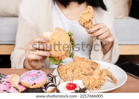  unhealthy woman over eating fast food burgers, fired chicken, donuts, and desserts,  Binge Eating Disorder (BED) concept  Royalty-Free Stock Photo #2257686005