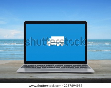Delivery truck flat icon on modern laptop computer screen on wooden table over tropical sea and blue sky with white clouds, Business transportation online service concept