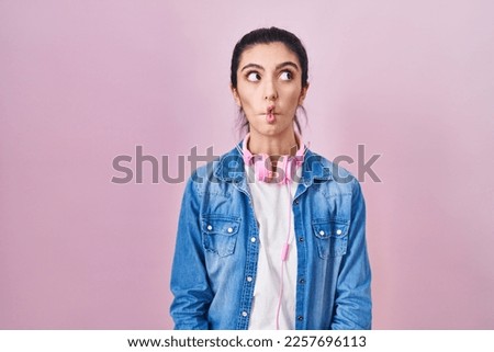 Young beautiful woman standing over pink background making fish face with lips, crazy and comical gesture. funny expression. 