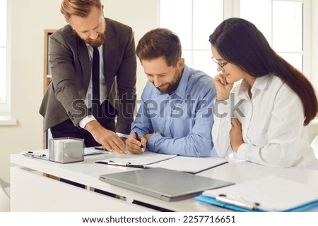 Young couple buying house and signing contract at real estate agent's office. Happy man and woman sitting at office table and putting signatures on contract agreement. Mortgage, buying house concept