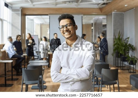 Portrait of happy Afro American business coach. Handsome young Black man in white shirt and eyeglasses standing in office after corporate team training class, looking at camera and smiling Royalty-Free Stock Photo #2257716657