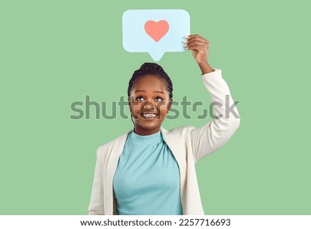 Smiling young black woman isolated on green studio background hold speech bubble with painted heart. Happy African American girl with talk balloon show love and care. Charity and volunteer.