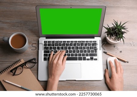Woman using laptop at wooden desk, top view. Device display with chroma key