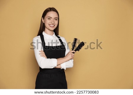 Portrait of happy hairdresser with brush and comb on beige background. Space for text Royalty-Free Stock Photo #2257730083