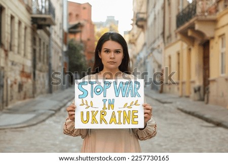 Sad woman holding poster Stop War in Ukraine on city street