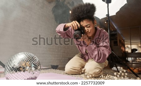 Black girl photographer taking photo of disco ball, jade roller, face brush, ice and blossom tree branch on digital camera at home studio. Creating content for photostocks, commerce and advertising