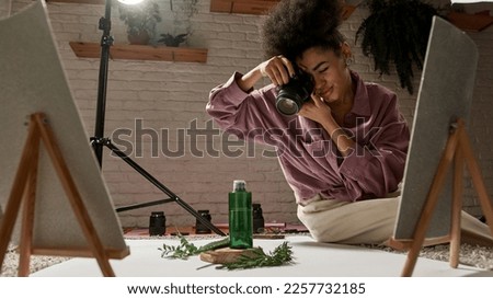 Black female photographer taking photo of aloe vera leaf, branches and lotion on this plants on digital camera at home studio. Beauty and body care content for photostocks, commerce, social networks