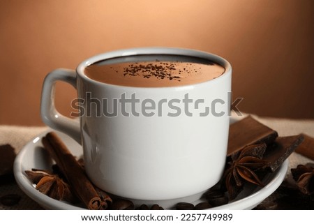 Cup of delicious hot chocolate, spices and coffee beans on table, closeup
