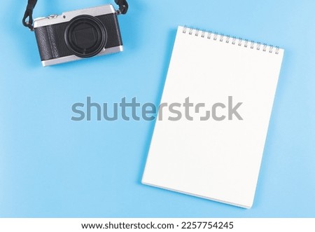 Top view or flat lay of blank page opened notebook and camera on blue background.
