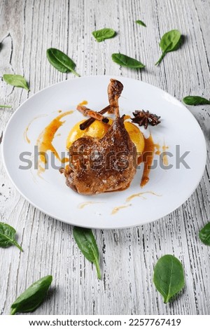 Duck leg Confit with apples in orange sauce on a white plate.