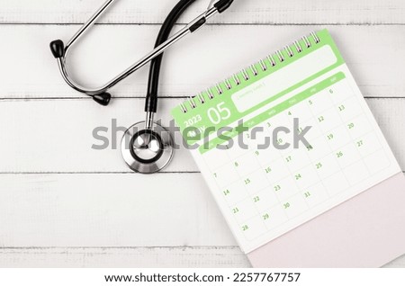 May 2023 desk calendar and stethoscope medical on wooden background, schedule to check up healthy concepts.