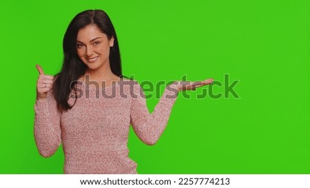 Lovely woman showing thumbs up and pointing empty place, advertising area for commercial text, copy space for goods promotion discount. Young pretty girl. Indoor studio shot on red wall background