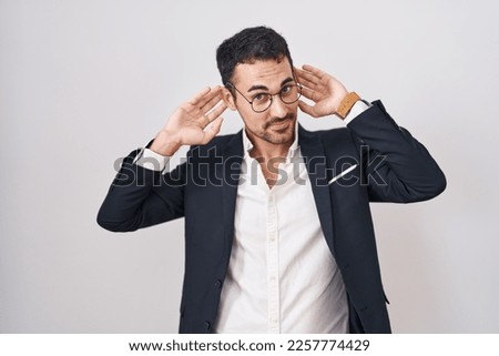 Handsome business hispanic man standing over white background smiling pulling ears with fingers, funny gesture. audition problem 