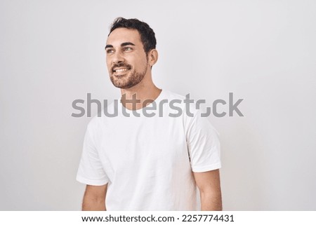 Handsome hispanic man standing over white background looking away to side with smile on face, natural expression. laughing confident. 