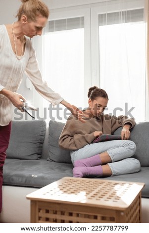 Mother having trouble with a lazy teenager girl at home while playing video games on a tablet and smartphone.