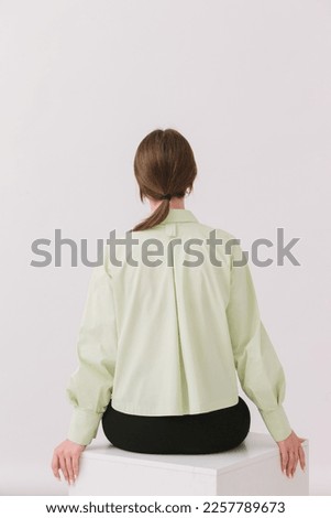 Photo of a beautiful woman in a colorful stylish shirt sitting on a white cube isolated on a white background. Shirt mockup.