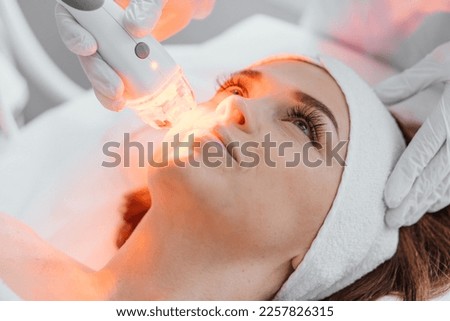 Red LED treatment. Woman doing facial skin therapy. Radiofrequency face lifting. Hardware antiaging procedure. RF lifting and vacuum massage. A cosmetologist performs a cosmetology procedure Royalty-Free Stock Photo #2257826315