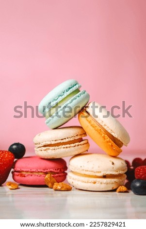 Colorful macarons. Small French cakes. Sweet and colorful french macaroons. Many tasty macarons with fresh berries, raspberries and blueberries, nuts and strawberries on a pink background Royalty-Free Stock Photo #2257829421