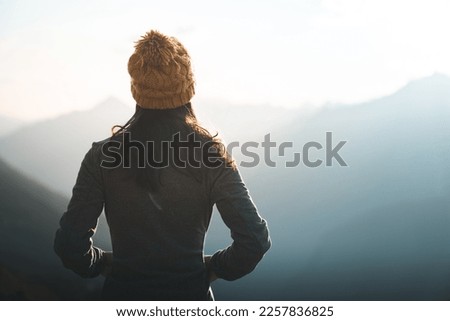 Close up of back view female hiker with knitted hat or beanie looking at mountain view. Young woman takes a moment to reflect and appreciate the beauty of nature. Scene of peace and serenity Royalty-Free Stock Photo #2257836825