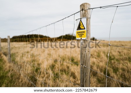 Shallow focus of a newly erected Danger sign and fence warning of cliff erosion with nearby houses falling into the sea.