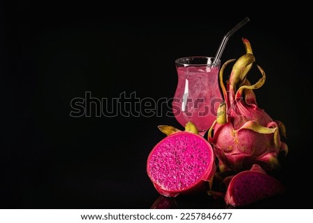 Glass of tasty pitahaya cocktail and fresh dragon fruits on dark background