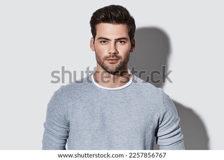Handsome young man in casual wear looking at camera while standing against grey background Royalty-Free Stock Photo #2257856767