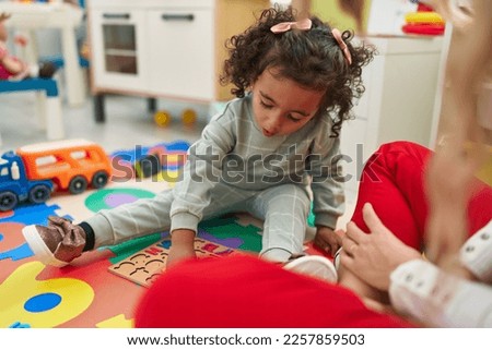Adorable hispanic girl playing with maths puzzle game sitting on floor at kindergarten Royalty-Free Stock Photo #2257859503