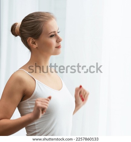 Young woman in white underwear is standing in front of the window and looking into it. Girl at home in the living room.
