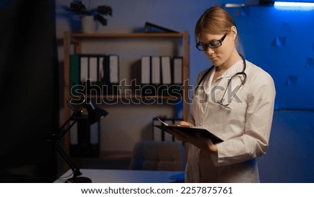 Attractive young female doctor in white coat in medical office during night shift. Copy space