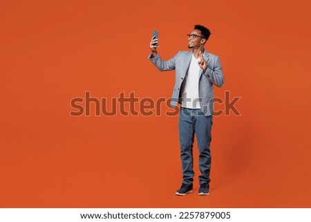 Full body young employee business man corporate lawyer wears classic formal grey suit shirt glasses work in office do selfie shot on mobile cell phone isolated on plain red orange background studio