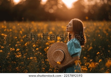 Portrait of attractive woman posing in blooming canola flowers field. Elegant girl in retro dress with straw hat, countryside nature place. Rapeseed meadow, vintage outfit, spring season Royalty-Free Stock Photo #2257892193