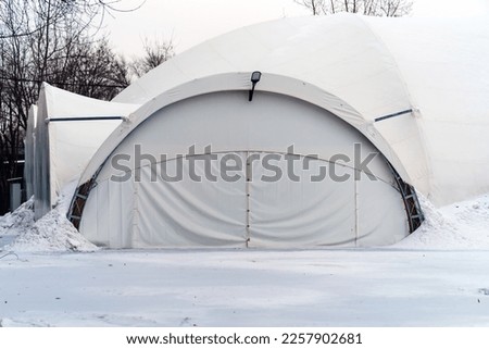 A large prefabricated hangar made of metal structures and synthetic film is covered with snow Royalty-Free Stock Photo #2257902681