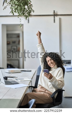 Euphoric young female worker holding mobile phone celebrating win receiving good news about job promotion, getting hired, feeling happy, rejoicing success with yes reaction working in office. Vertical Royalty-Free Stock Photo #2257912239