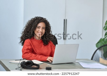 Young happy pretty latin business woman company worker sitting at desk working on laptop. Smiling female professional executive using computer in corporate office looking at camera. Portrait. Royalty-Free Stock Photo #2257912247