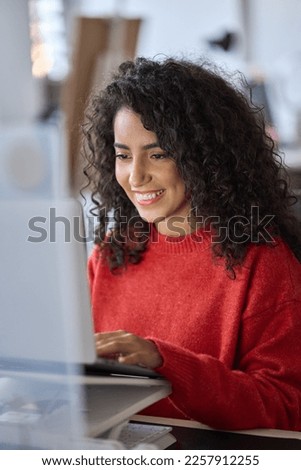 Young happy latin business woman office worker, company employee or student using laptop, typing on computer sitting at desk in office watching online webinar, elearning course looking at pc. Vertical