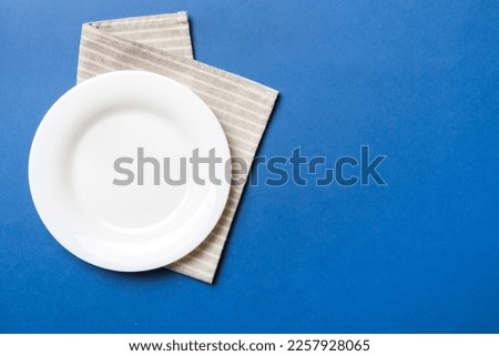 Top view on colored background empty round white plate on tablecloth for food. Empty dish on napkin with space for your design. Royalty-Free Stock Photo #2257928065