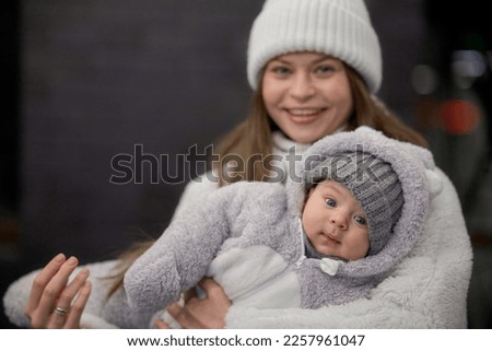 young woman with a baby in her arms walking around the city. mom and son are walking in cold weather, dressed in trendy warm clothes. Mom gently hugs her child.