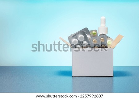 Cardboard box with different medicine pills, tablets and capsules on a blue background with copy space. Buying drug delivery concept. Royalty-Free Stock Photo #2257992807