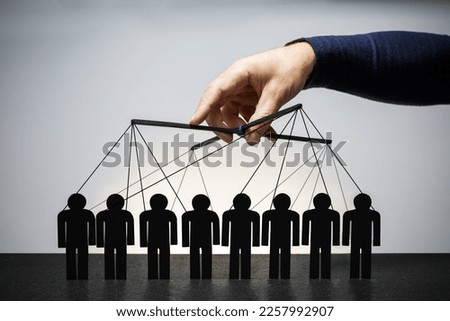 Manipulation concept. Male hand, puppeteer controls figure of peoples. Manipulation of people.  Royalty-Free Stock Photo #2257992907