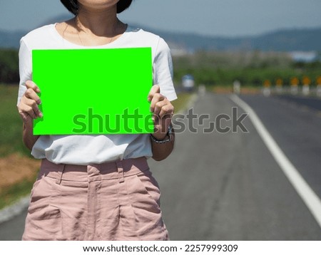 Woman holding a green copy paper. On the street. Space for advertisement.