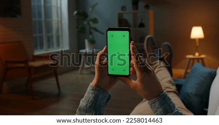 Close up shot of guy lying on couch at night, holding a smartphone with chroma key mock up green screen - technology, connections, communications concept 