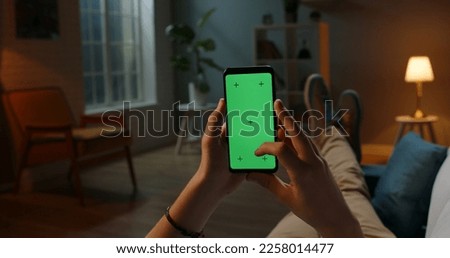 Man lying on couch using smartphone with chroma key green screen at night, scrdoing various gestures like swiping and scrolling - internet, communications concept close up 