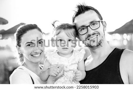 Family picture of smiling young mom and dad posing in beach with cute little daughter - Summer party