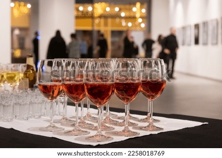 Row of Glasses filled with Wine in the background of blurred people and framed paintings at the exhibition in modern gallery. Artwork blurred in the background. Art gallery hall.