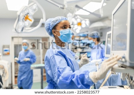 Anesthetist Working In Operating Theatre Wearing Protecive Gear checking monitors while sedating patient before surgical procedure in hospital Royalty-Free Stock Photo #2258023577