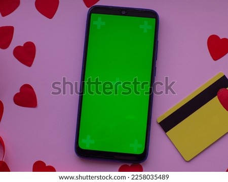 Phone with chroma key screen and credit card on pink background. Red heart paper on pastel pink background, top view with copy space. Greeting card. Valentines day shopping concept. February 14th. 